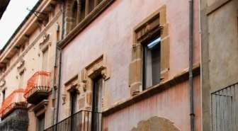 Façana rosada de Casa Joan, amb finestres emmarcades en pedra tallada, un balcó de barana de ferro i l'arrebossat envellit