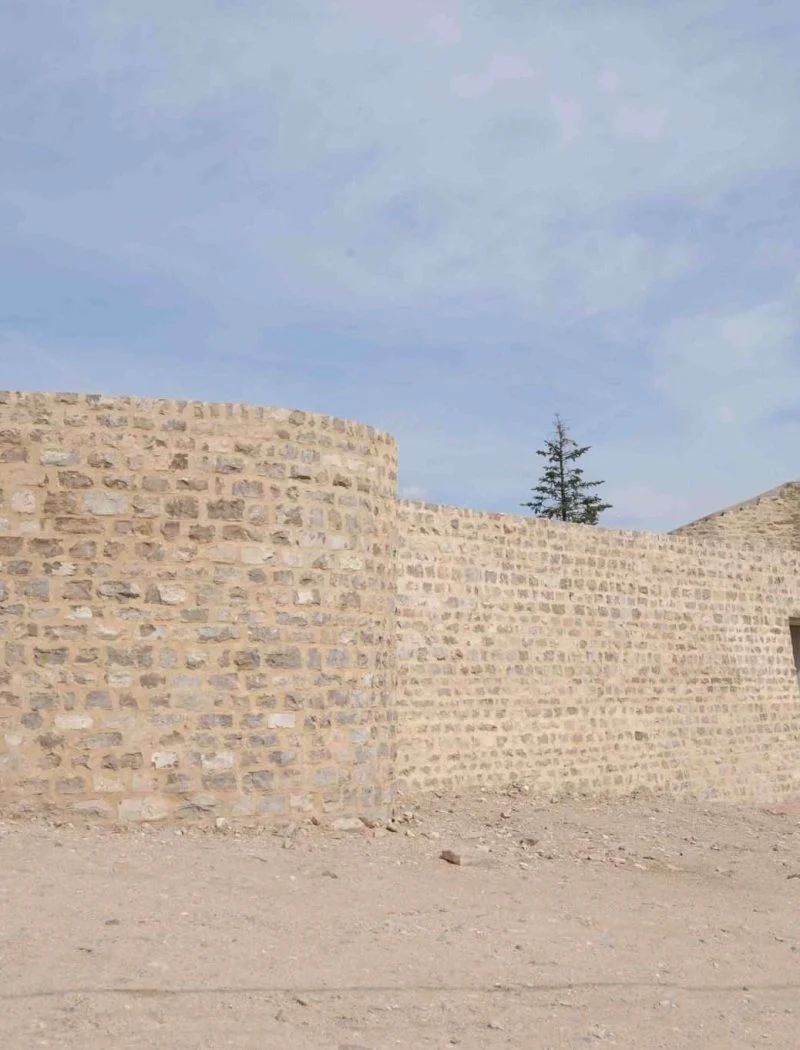 Restes del castell de Cervera: el mur exterior de pedra amb un bastió de planta corba i un portal obert, sobre l'esplanada de terra del turó de Montseré
