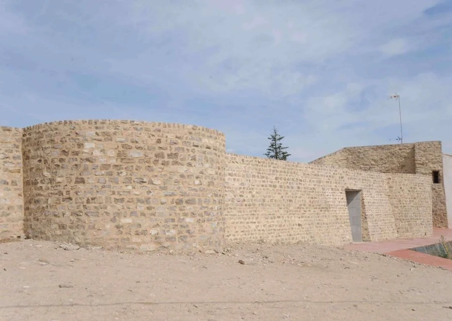 Restes del castell de Cervera: el mur exterior de pedra amb un bastió de planta corba i un portal obert, sobre l'esplanada de terra del turó de Montseré