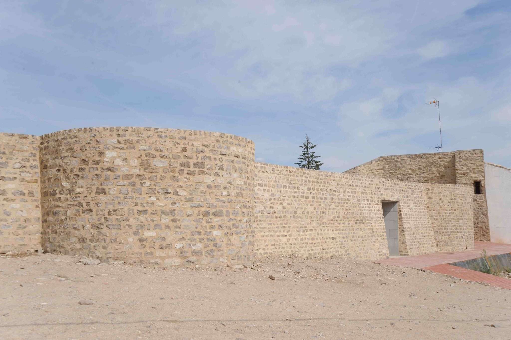 Restes del castell de Cervera: el mur exterior de pedra amb un bastió de planta corba i un portal obert, sobre l'esplanada de terra del turó de Montseré