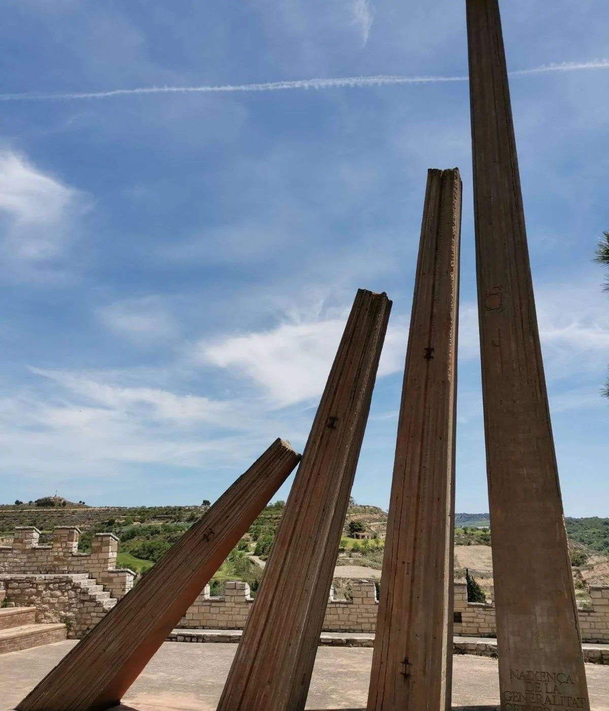 Monument a la Generalitat, de Josep M. Subirachs: quatre pilars metàl·lics inclinats de diferents alçades sobre una plataforma pavimentada, amb el paisatge de la Segarra al fons