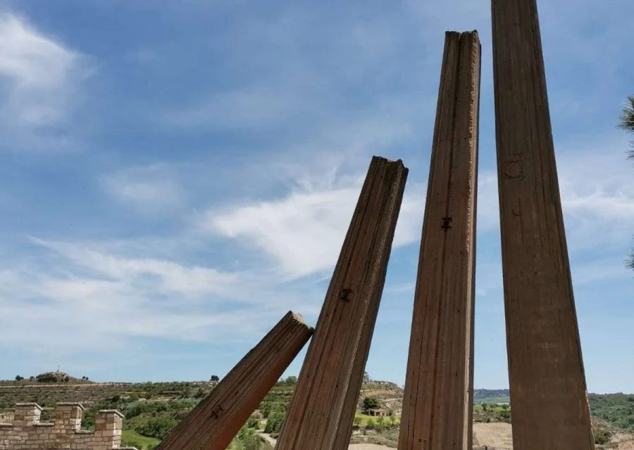 Monument a la Generalitat, de Josep M. Subirachs: quatre pilars metàl·lics inclinats de diferents alçades sobre una plataforma pavimentada, amb el paisatge de la Segarra al fons