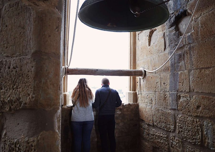 Dues persones d'esquena s'aboquen a la finestra del campanar de Santa Maria de Cervera per contemplar la panoràmica, amb una campana de bronze penjada al damunt