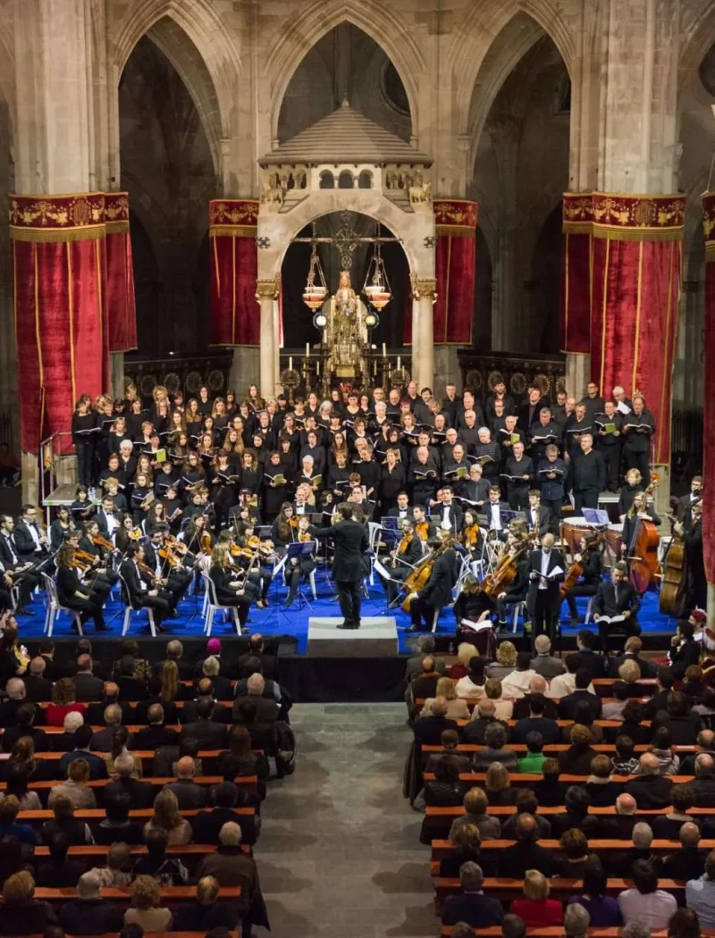 Concert de completes de la Festa Major del Santíssim Misteri a l'església de Santa Maria de Cervera, amb l'orquestra i el cor davant l'altar, cortinatges vermells i el temple ple de públic