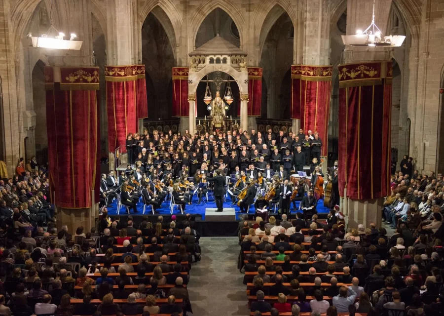 Concert de completes de la Festa Major del Santíssim Misteri a l'església de Santa Maria de Cervera, amb l'orquestra i el cor davant l'altar, cortinatges vermells i el temple ple de públic