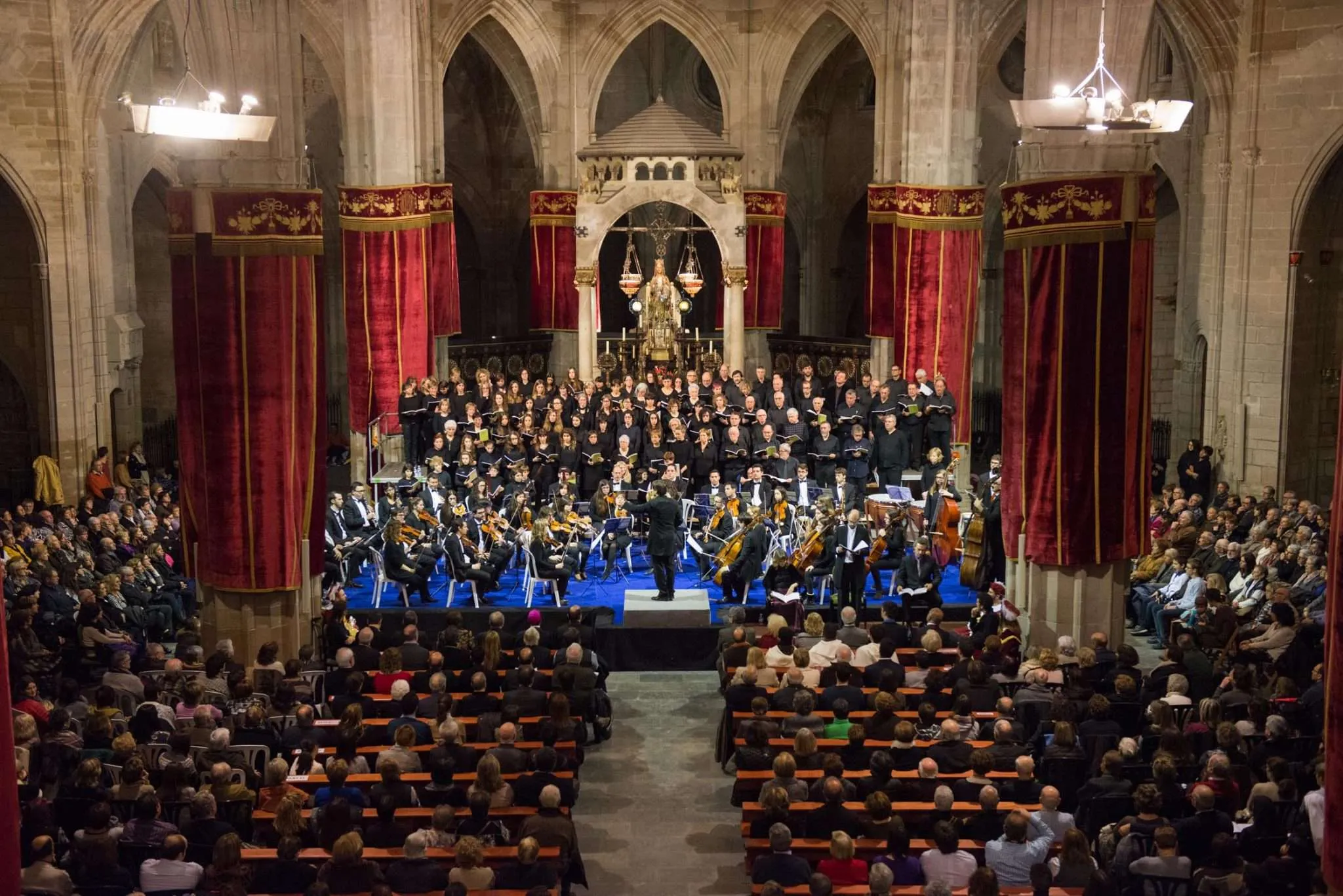Concert de completes de la Festa Major del Santíssim Misteri a l'església de Santa Maria de Cervera, amb l'orquestra i el cor davant l'altar, cortinatges vermells i el temple ple de públic