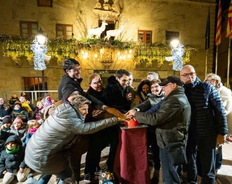 Encesa dels llums de Nadal a Cervera: un grup de persones prem alhora el polsador davant de la façana de la Paeria guarnida amb garlandes i rens lluminosos, amb la canalla mirant