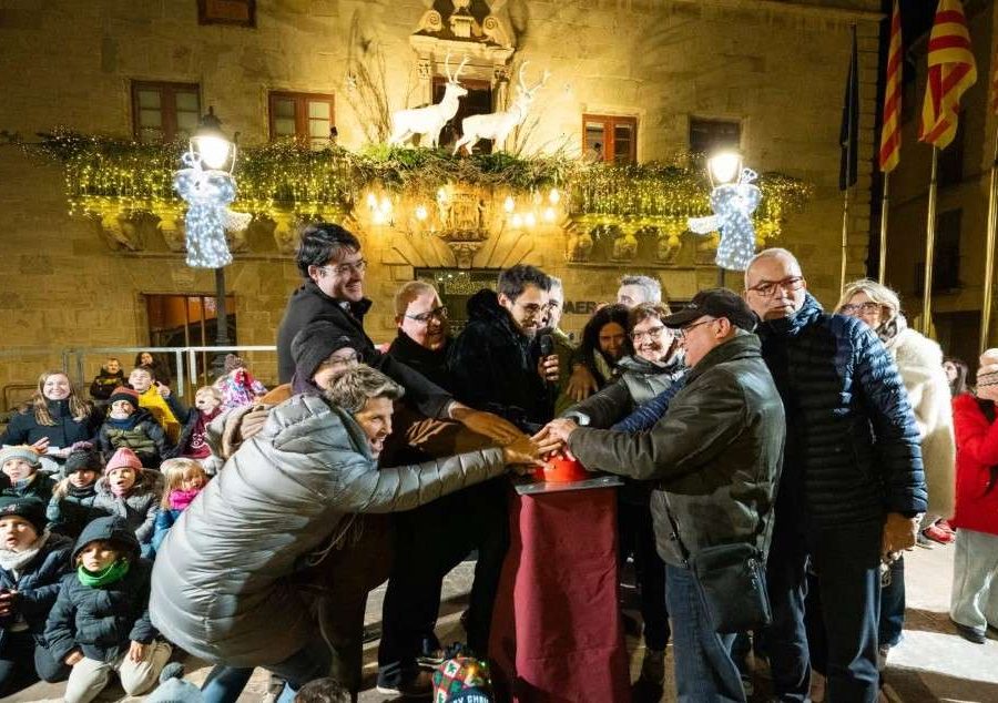 Encesa dels llums de Nadal a Cervera: un grup de persones prem alhora el polsador davant de la façana de la Paeria guarnida amb garlandes i rens lluminosos, amb la canalla mirant