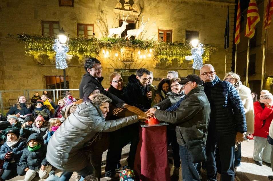 Encesa dels llums de Nadal a Cervera: un grup de persones prem alhora el polsador davant de la façana de la Paeria guarnida amb garlandes i rens lluminosos, amb la canalla mirant