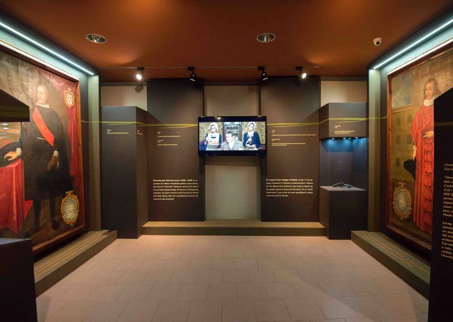 Sala d'exposició del Museu Comarcal de Cervera, amb dos grans retrats històrics emmarcats als murs laterals, plafons de text i una pantalla de vídeo al centre