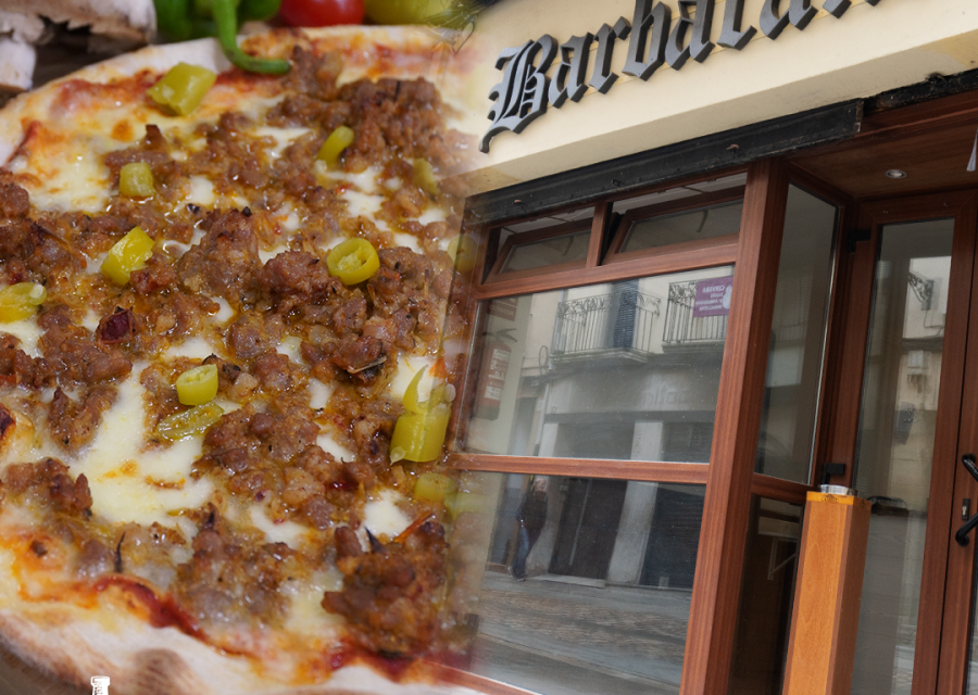 Composició de la Pizzeria Barbacana: una pizza amb carn i pebrots damunt una post de fusta i, a la dreta, la porta d'entrada del local amb el rètol Barbacana