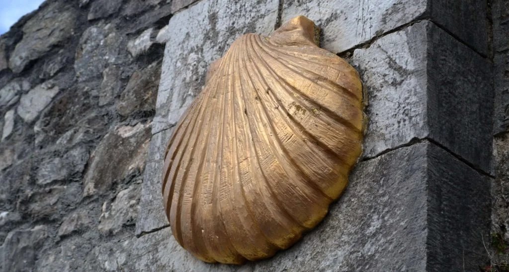Petxina daurada del Camí de Sant Jaume fixada sobre un mur de pedra.