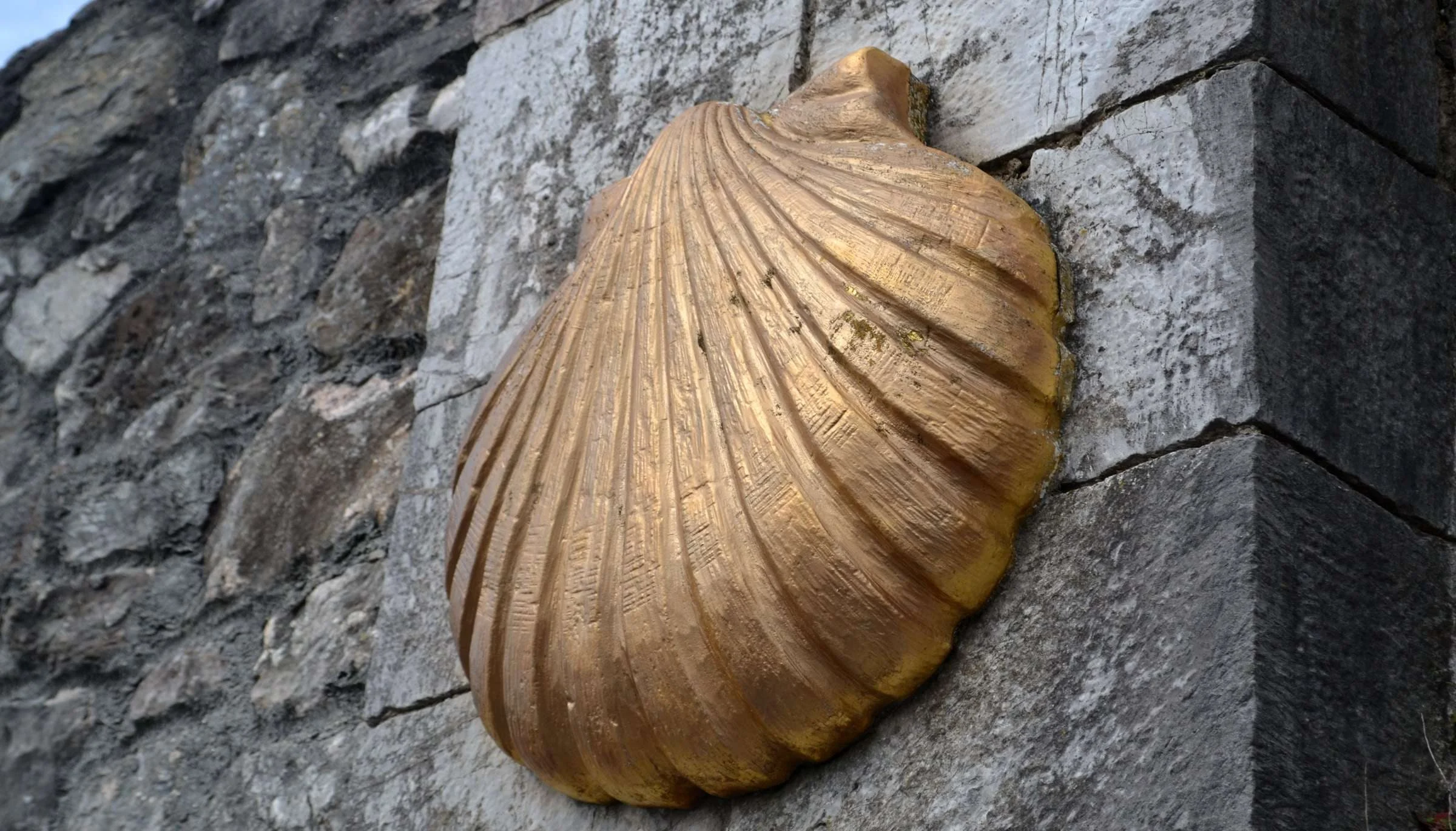Petxina daurada del Camí de Sant Jaume fixada sobre un mur de pedra.