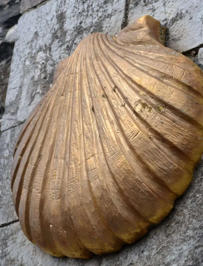 Petxina daurada del Camí de Sant Jaume fixada sobre un mur de pedra.