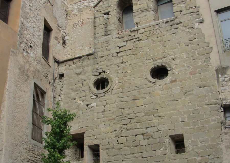 Façana de pedra de l’antiga església de Sant Joan de Jerusalem de Cervera, amb finestres romàniques i bancs a la plaça.