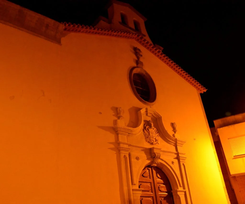 Façana de l’església de Sant Magí de Cervera il·luminada de nit, amb portal escultòric, rosassa i campanar.