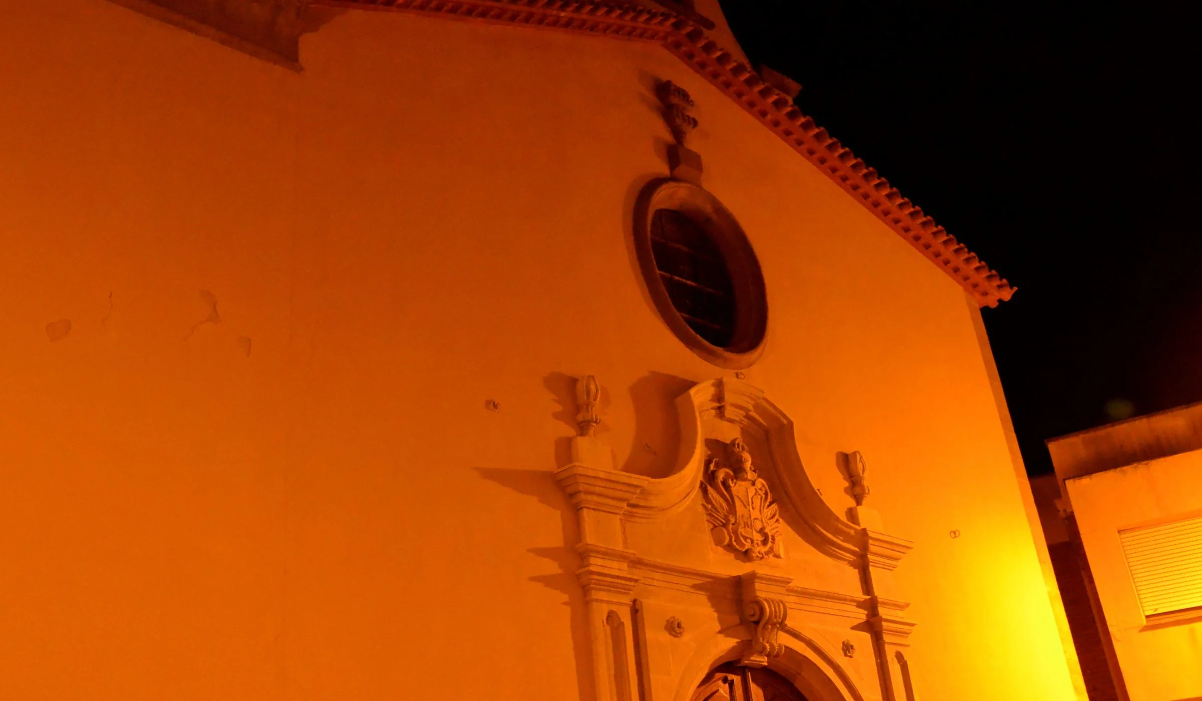 Façana de l’església de Sant Magí de Cervera il·luminada de nit, amb portal escultòric, rosassa i campanar.