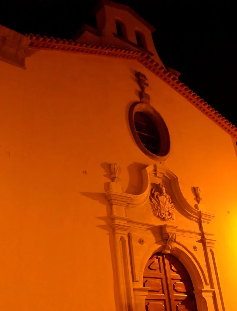 Façana de l’església de Sant Magí de Cervera il·luminada de nit, amb portal escultòric, rosassa i campanar.