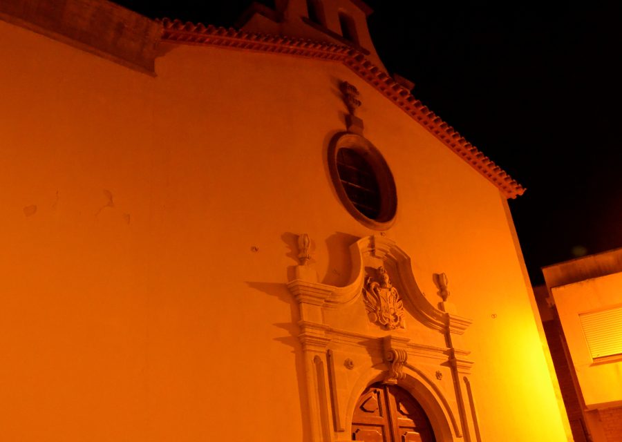 Façana de l’església de Sant Magí de Cervera il·luminada de nit, amb portal escultòric, rosassa i campanar.