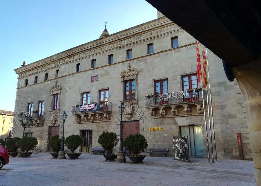 Façana de pedra de la Paeria de Cervera, amb balcons esculpits, testos a la plaça i un porxo en primer terme.