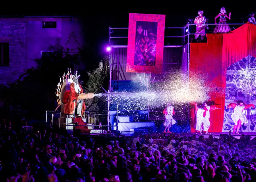 Escena nocturna de l’Aquelarre de Cervera, amb intèrprets en una estructura elevada, llum violeta i una plaça plena de públic.