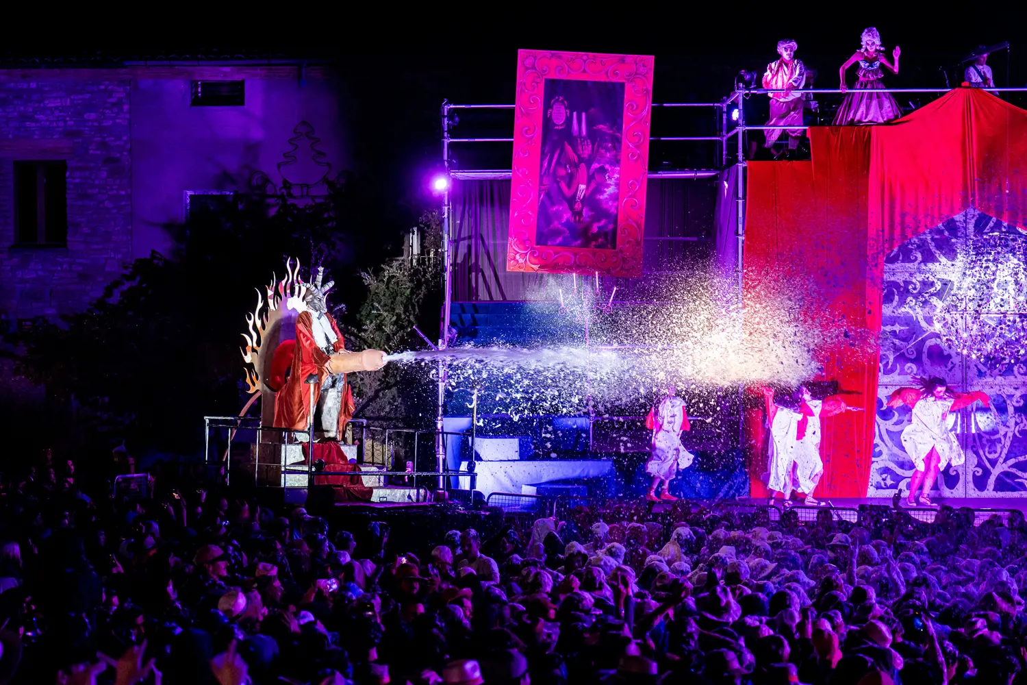 Escena nocturna de l’Aquelarre de Cervera, amb intèrprets en una estructura elevada, llum violeta i una plaça plena de públic.
